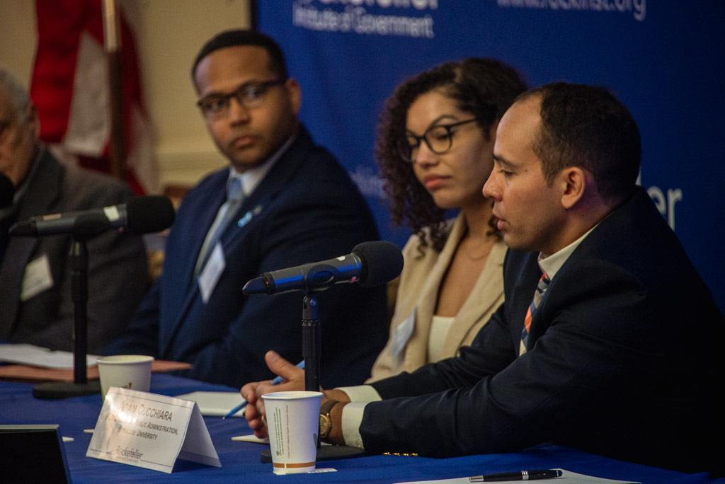 Three scholars seated at a table present research in front of a Rockefeller Institute of Government banner.